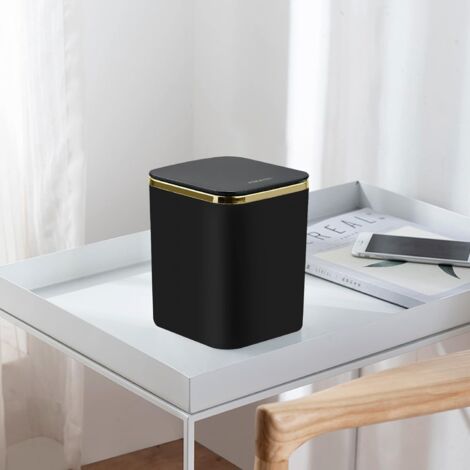 Black small desktop trash can with gold ring accent on modern white desk lifestyle setting
