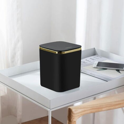 Black small desktop trash can with gold ring accent on modern white desk lifestyle setting
